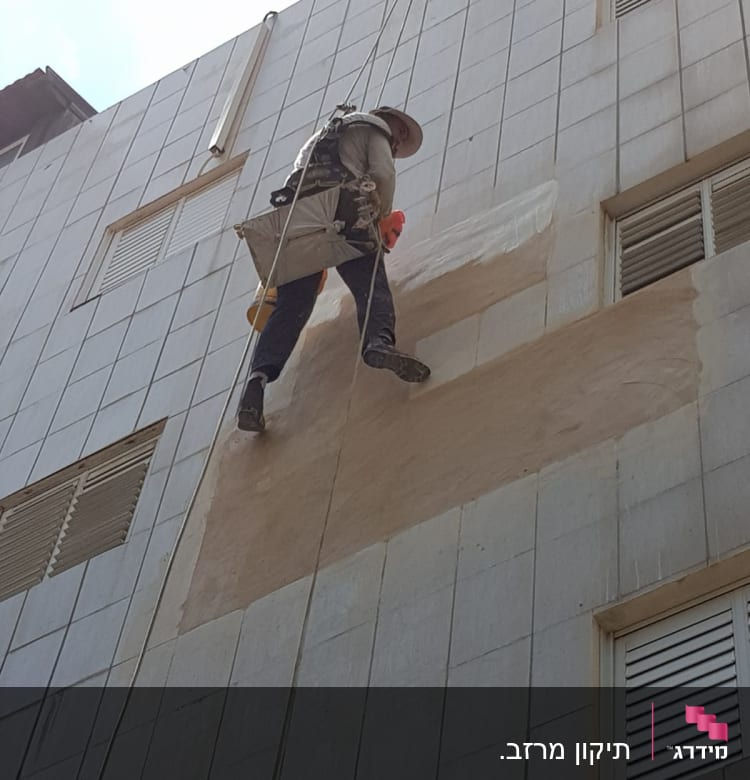 אדם על חבלים צובע קיר חיצוני של בניין